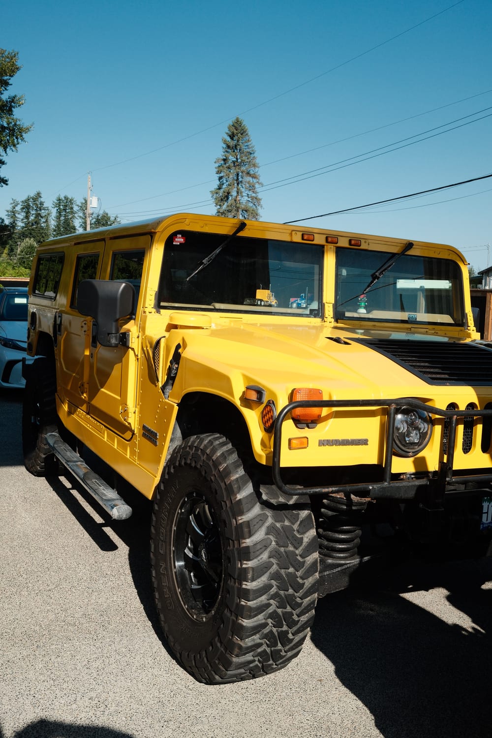 A bright yellow Hummer H1 parked in sunlight, with a black brush guard, black wheels and mud terrain tyres.
